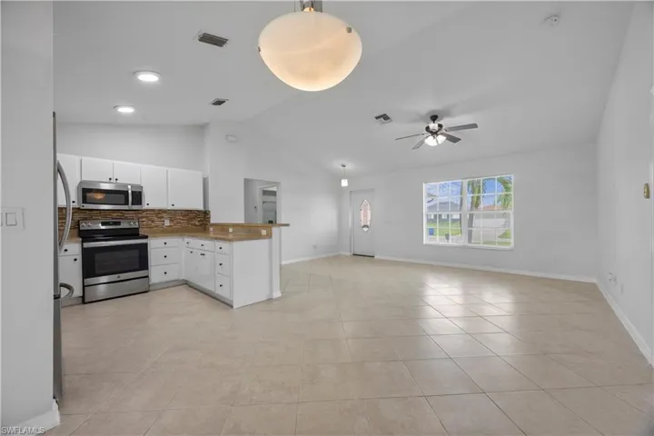 Kitchen with appliances with stainless steel finishes, a peninsula, open floor plan, vaulted ceiling, and light tile patterned floors