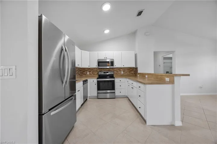 Kitchen featuring appliances with stainless steel finishes, a peninsula, vaulted ceiling, light tile patterned floors, and decorative backsplash
