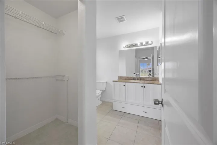 Bathroom with vanity, toilet, a walk in closet, tile patterned flooring, and baseboards