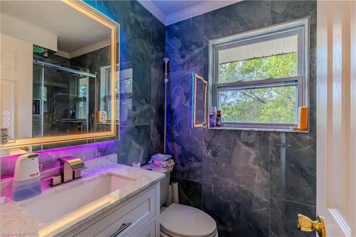 Bathroom with crown molding, vanity, toilet, and an enclosed shower