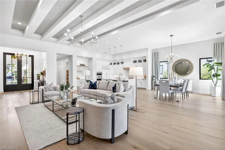 The large great room with open an concept family style design is bright and airy ,lovely wood floors, beamed ceiling, contemporary chandeliars and plenty  of natural lighit flows through the 10 ft high double front doors