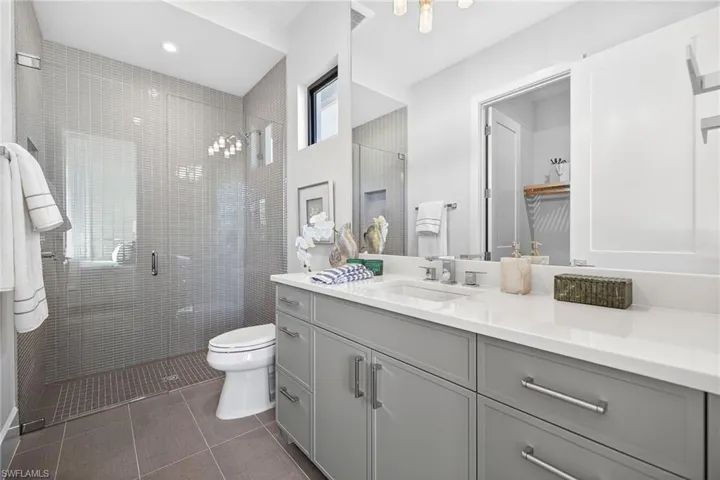Guest bathroom 1 with a large tiled shower stall, large vanity, and dark tile patterned floors