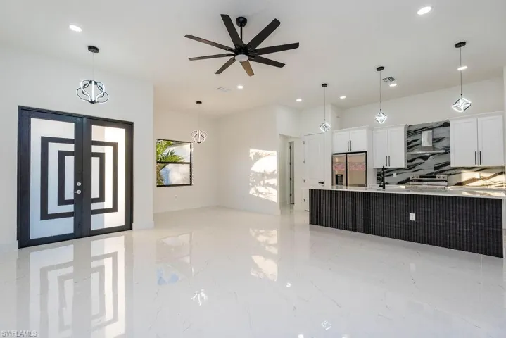Kitchen featuring white cabinets, pendant lighting, open floor plan, stainless steel fridge, and wall chimney range hood