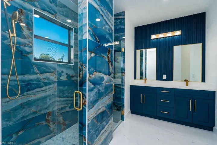 Bathroom with double vanity, a marble finish shower, light marble finish floors, and recessed lighting