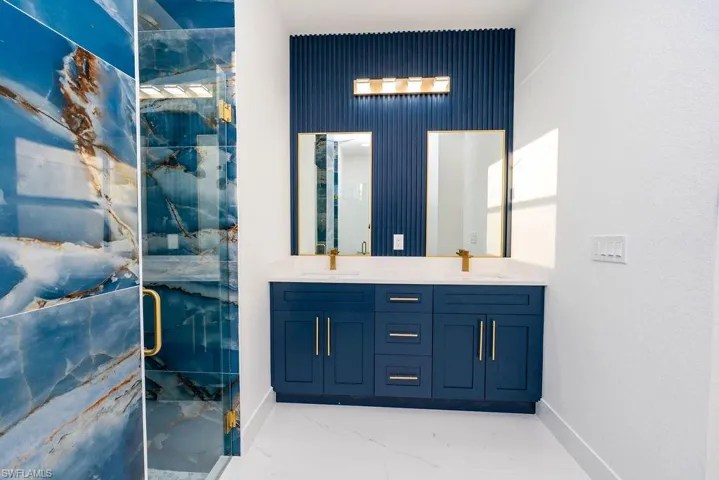 Full bathroom featuring a marble finish shower, double vanity, and light marble finish floors