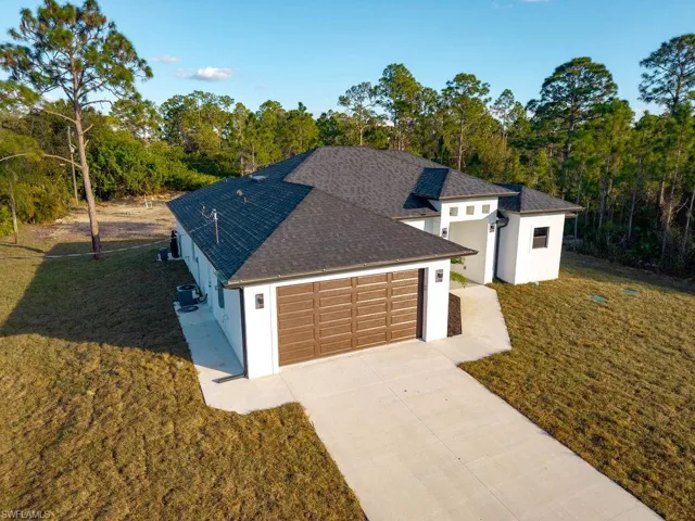 View of front of house with a front lawn, stucco siding, a shingled roof, and driveway