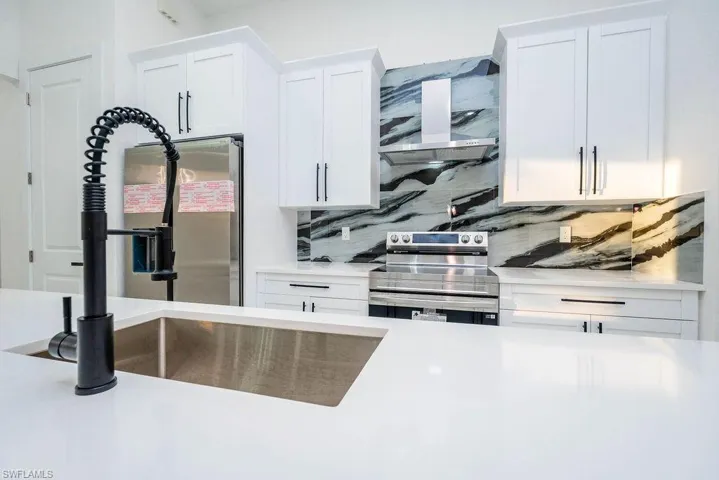 Kitchen with white cabinets, electric range, backsplash, and light stone counters