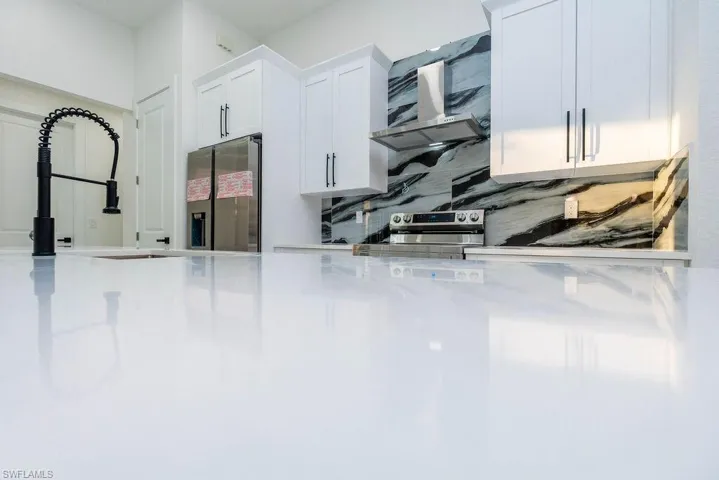 Kitchen featuring white cabinetry, appliances with stainless steel finishes, decorative backsplash, and light stone counters