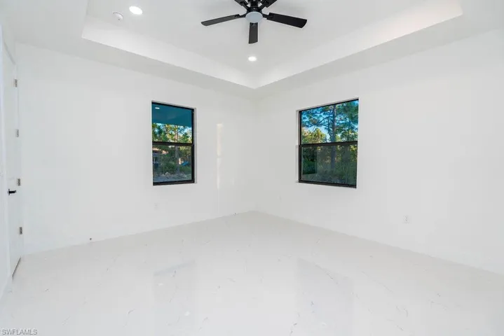 Empty room with a raised ceiling, recessed lighting, and marble tiled flooring
