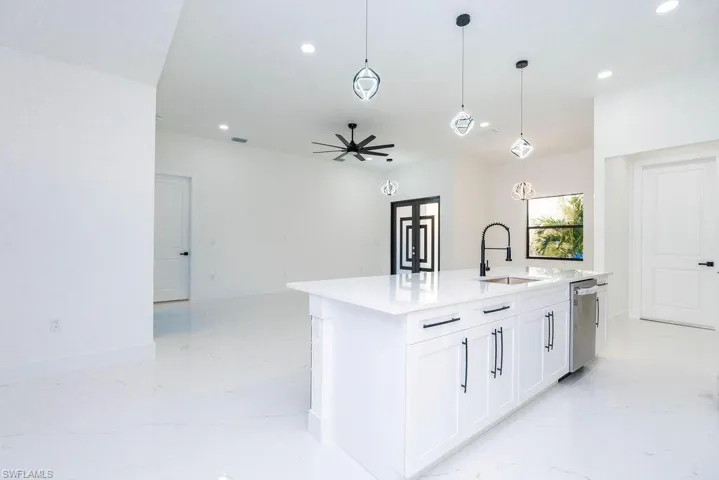Kitchen with decorative light fixtures, white cabinets, a kitchen island with sink, light stone counters, and ceiling fan