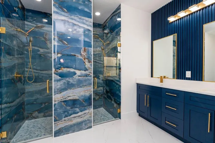 Full bathroom featuring a marble finish shower, double vanity, light marble finish floors, and recessed lighting