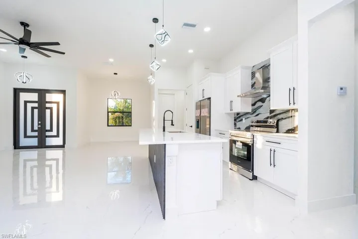 Kitchen featuring stainless steel appliances, white cabinetry, a kitchen island with sink, decorative light fixtures, and wall chimney range hood