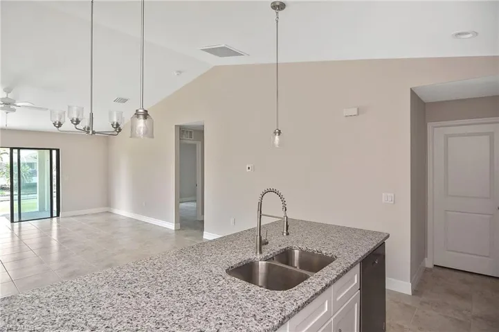 Kitchen with light tile patterned floors, white cabinets, light stone countertops, decorative light fixtures, and a ceiling fan