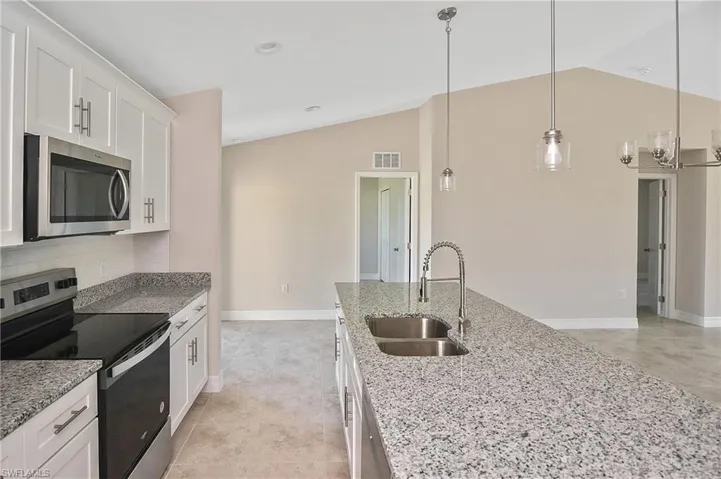Kitchen featuring appliances with stainless steel finishes, decorative light fixtures, lofted ceiling, white cabinets, and light stone counters