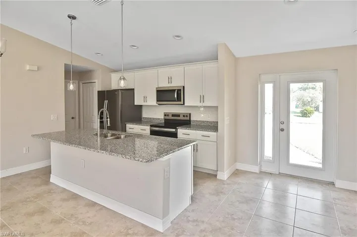 Kitchen with appliances with stainless steel finishes, light stone counters, decorative backsplash, a kitchen island with sink, and pendant lighting