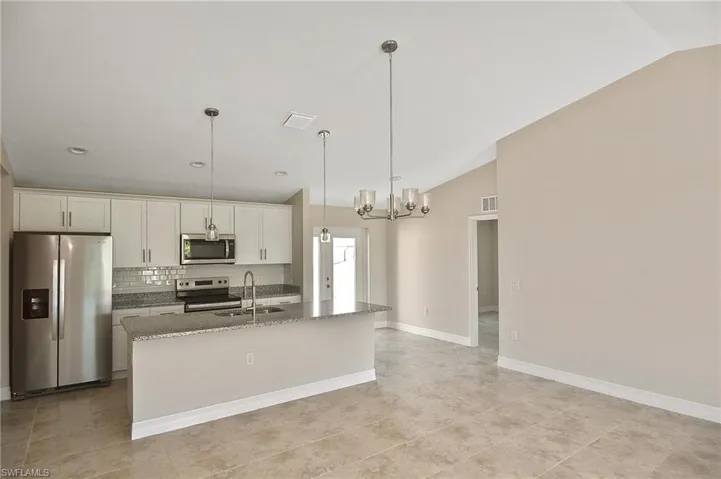 Kitchen with appliances with stainless steel finishes, decorative light fixtures, light stone counters, backsplash, and a chandelier