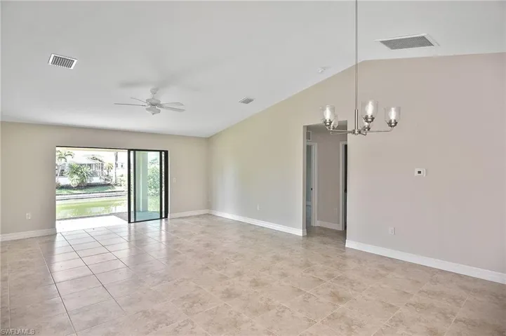 Empty room featuring vaulted ceiling, a chandelier, ceiling fan, and light tile patterned floors