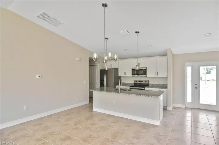 Kitchen with pendant lighting, dark stone countertops, stainless steel appliances, an island with sink, and white cabinetry