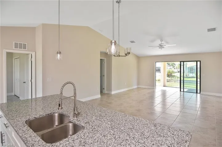 Kitchen with light stone countertops, lofted ceiling, light tile patterned floors, pendant lighting, and ceiling fan