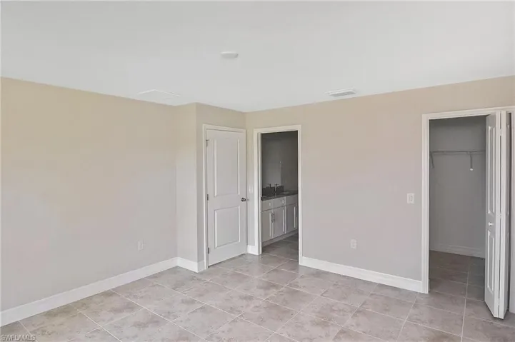 Unfurnished bedroom featuring a spacious closet, light tile patterned flooring, and ensuite bathroom