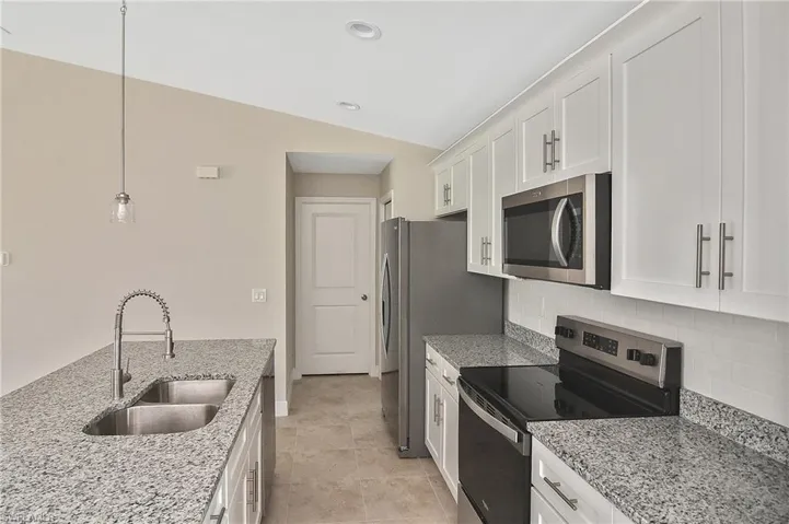 Kitchen featuring stainless steel appliances, hanging light fixtures, light stone countertops, white cabinets, and lofted ceiling