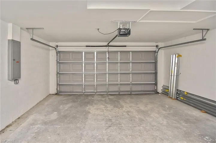 Garage with electric panel, concrete block wall, and a garage door opener