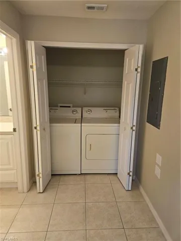 Washroom with light tile patterned floors, washer and clothes dryer, and electric panel