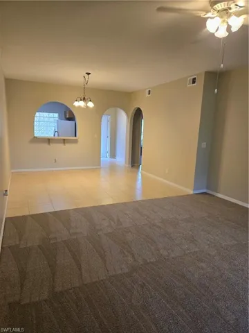 Carpeted empty room featuring ceiling fan with notable chandelier