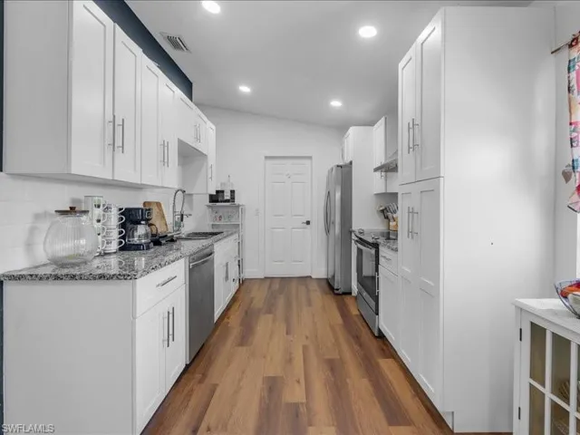 Galley-style kitchen featuring wood-finish flooring, white cabinetry, integrated stainless steel appliances, speckled countertops, and recessed lighting