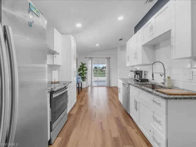 Kitchen featuring white shaker cabinetry, granite-style countertops, stainless steel appliances, wood-finish flooring, and recessed lighting