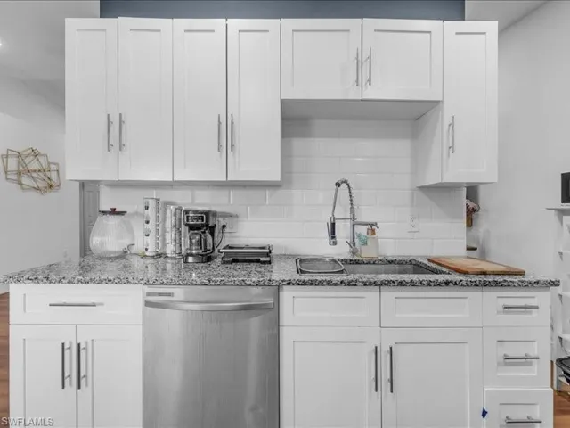 Kitchen featuring white shaker-style cabinetry with brushed nickel hardware, granite countertops, white subway tile backsplash, stainless steel dishwasher, and a gooseneck faucet