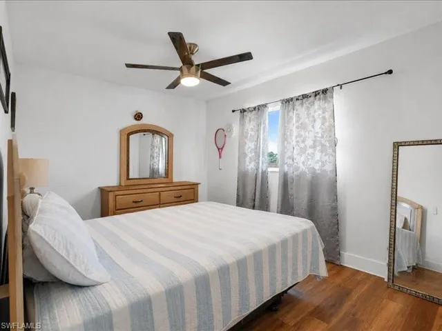 Bedroom featuring wood-finish flooring, a ceiling fan with integrated lighting, and a window with a curtain rod