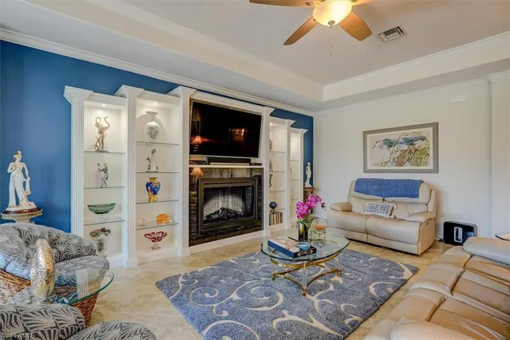 Living room featuring crown molding, ceiling fan, a fireplace, and a raised ceiling
