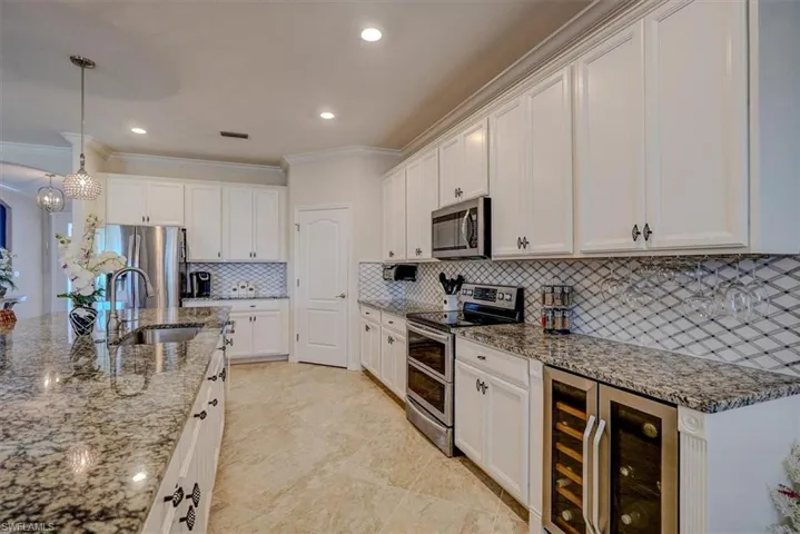 Kitchen featuring sink, hanging light fixtures, stainless steel appliances, beverage cooler, and white cabinets