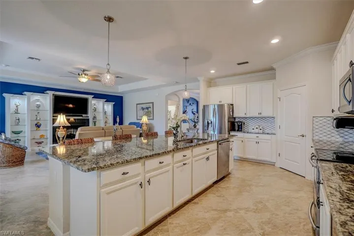 Kitchen with stone countertops, sink, hanging light fixtures, stainless steel appliances, and a center island with sink