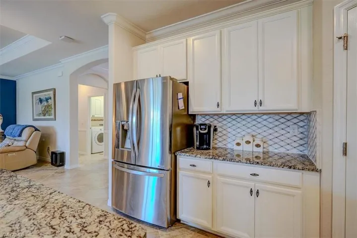 Kitchen with stainless steel refrigerator with ice dispenser, washer / dryer, crown molding, stone countertops, and decorative backsplash