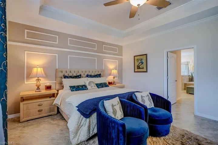 Tiled bedroom featuring a raised ceiling, ornamental molding, and ceiling fan