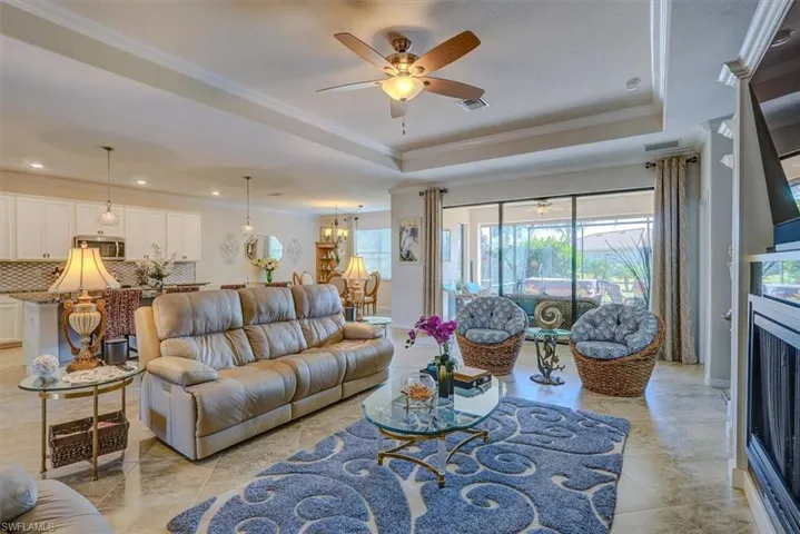 Tiled living room featuring crown molding, a raised ceiling, and ceiling fan with notable chandelier