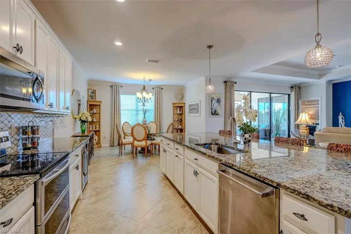 Kitchen with crown molding, pendant lighting, stainless steel appliances, light stone countertops, and white cabinets