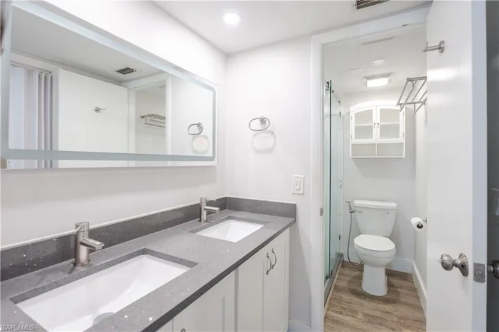 Full bath with double vanity, a stall shower, light wood-type flooring, and recessed lighting