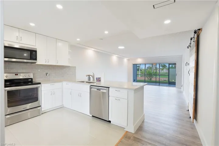 Kitchen with stainless steel appliances, a peninsula, open shelves, white cabinets, and decorative backsplash