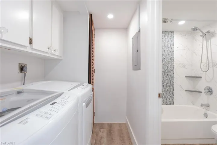 Laundry area featuring light wood-type flooring, electric panel, independent washer and dryer, recessed lighting, and cabinet space