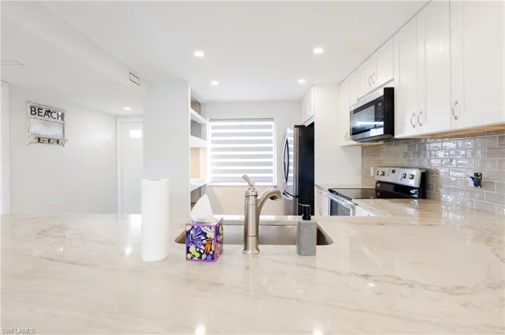 Kitchen featuring stainless steel appliances, light stone countertops, white cabinets, tasteful backsplash, and recessed lighting