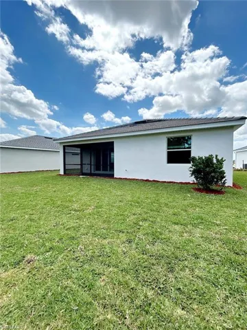 Back of house with a yard, stucco siding, and a sunroom