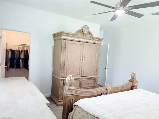 Bedroom with a walk in closet, wood finish floors, and ceiling fan