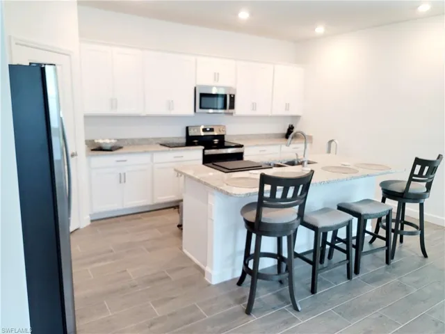 Kitchen with stainless steel appliances, a kitchen breakfast bar, wood finish floors, white cabinetry, and recessed lighting