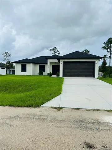 View of front of property with an attached garage, stucco siding, driveway, a front yard, and a shingled roof
