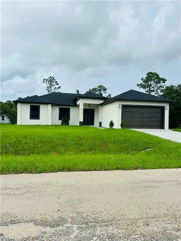 View of front facade featuring concrete driveway, stucco siding, an attached garage, a front yard, and a shingled roof