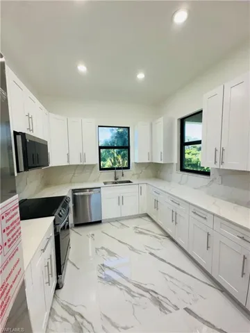 Kitchen with light marble finish floors, backsplash, white cabinetry, light stone countertops, and recessed lighting