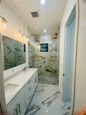 Bathroom with light marble finish floors, a marble finish shower, double vanity, and recessed lighting
